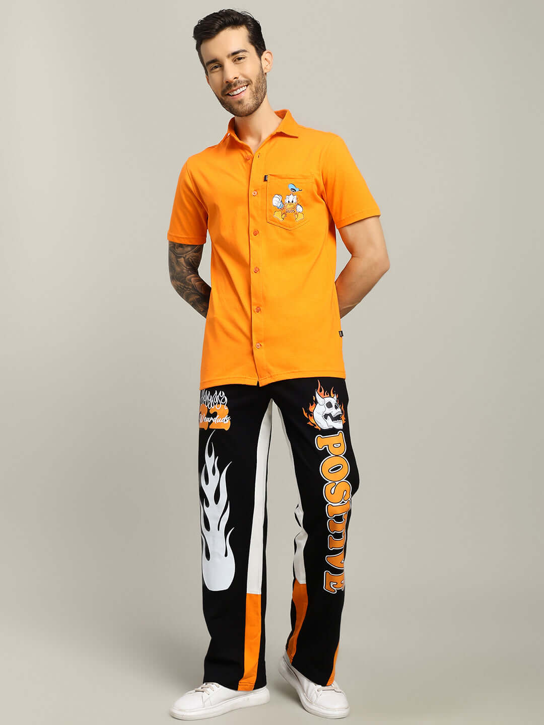 Man wearing DELLA REGULAR FIT SHIRT ORANGE with custom graphic pants, hands in pockets, casual fashion look.