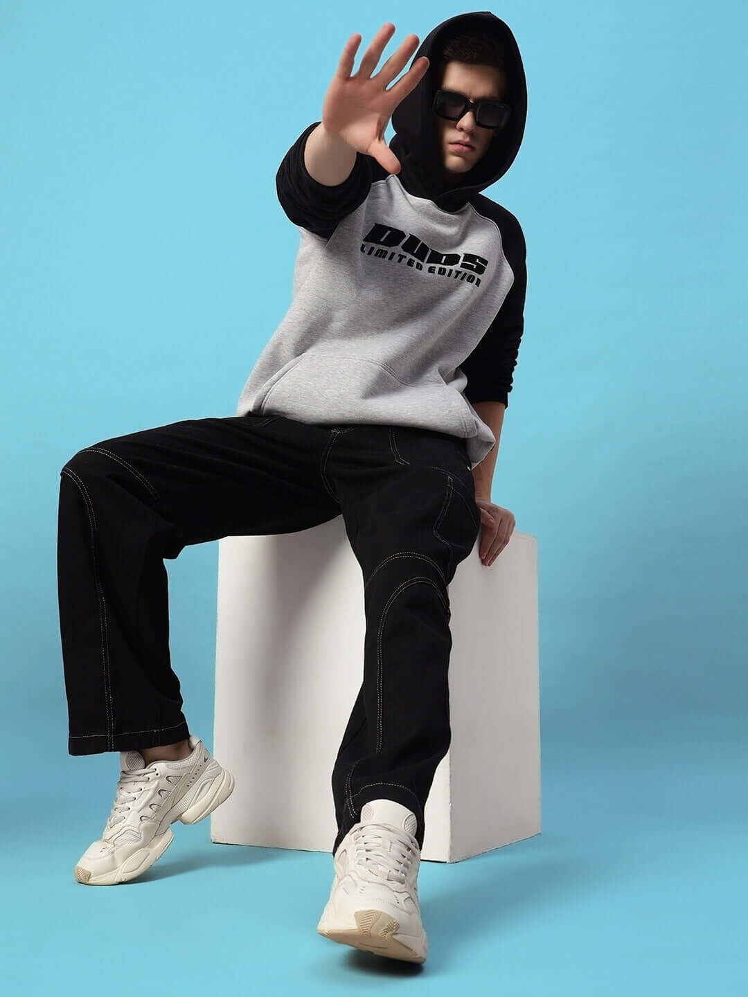 Model wearing DELUXE FLEECE COLORBLOCK OVERSIZE HOODIE BLACK MELANGE GREY in a stylish pose against a blue background.