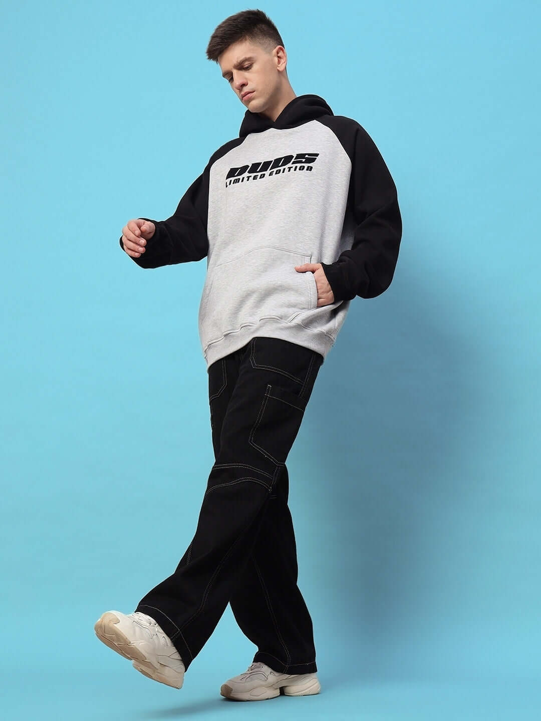 Model wearing DELUXE FLEECE COLORBLOCK OVERSIZE HOODIE BLACK MELANGE GREY against blue background.