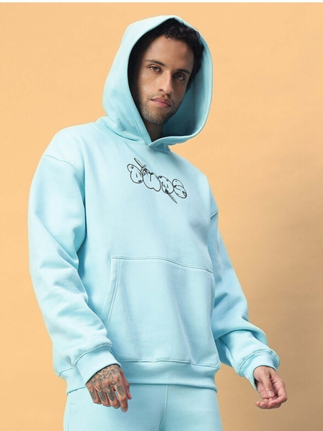 Model wearing WEARDUDS DEMON FLEECE CO-ORD SKY BLUE with hood up, displaying comfortable fit in a pastel setting.