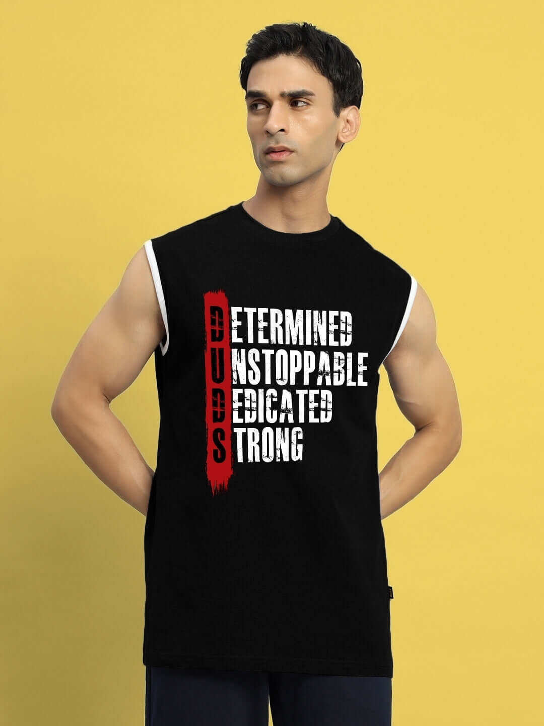 Man wearing DETERMINED PRINT GYM T-SHIRT BLACK with motivational text on front, sleeveless design, yellow background.