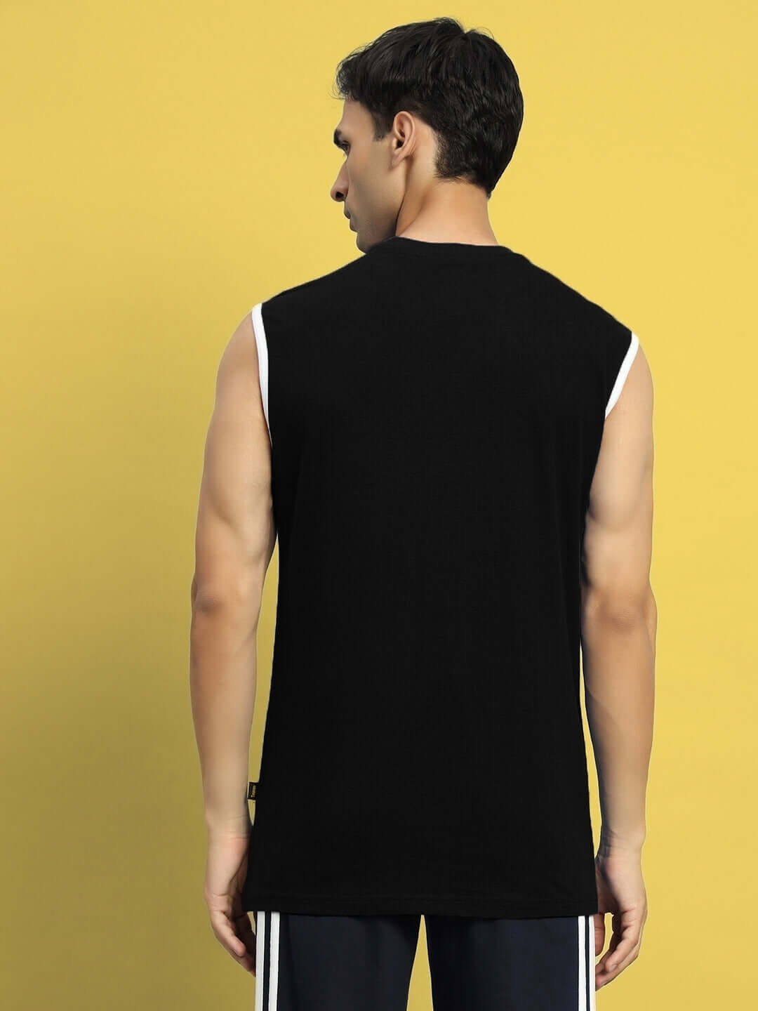 Back view of DETERMINED PRINT GYM T-SHIRT BLACK worn by a model, showcasing the sleeveless design and fit, against a yellow background.