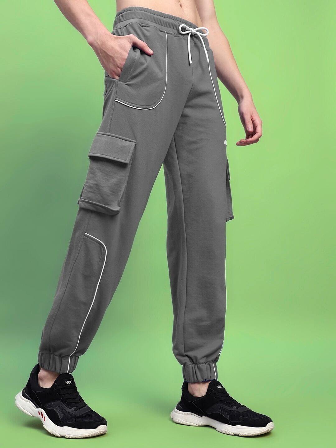 Model wearing DEVENO RELAXED-FIT JOGGERS GREY with adjustable waistband, side pockets, and black sneakers against green background.