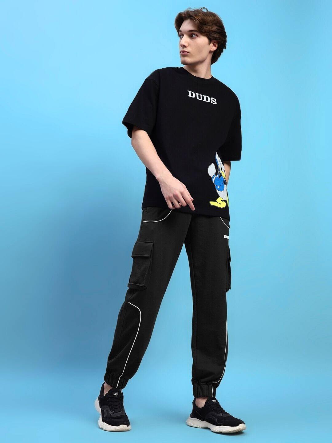 Model wearing DEVENO relaxed-fit black joggers by DUDS, styled with a black T-shirt, showcasing casual streetwear fashion.