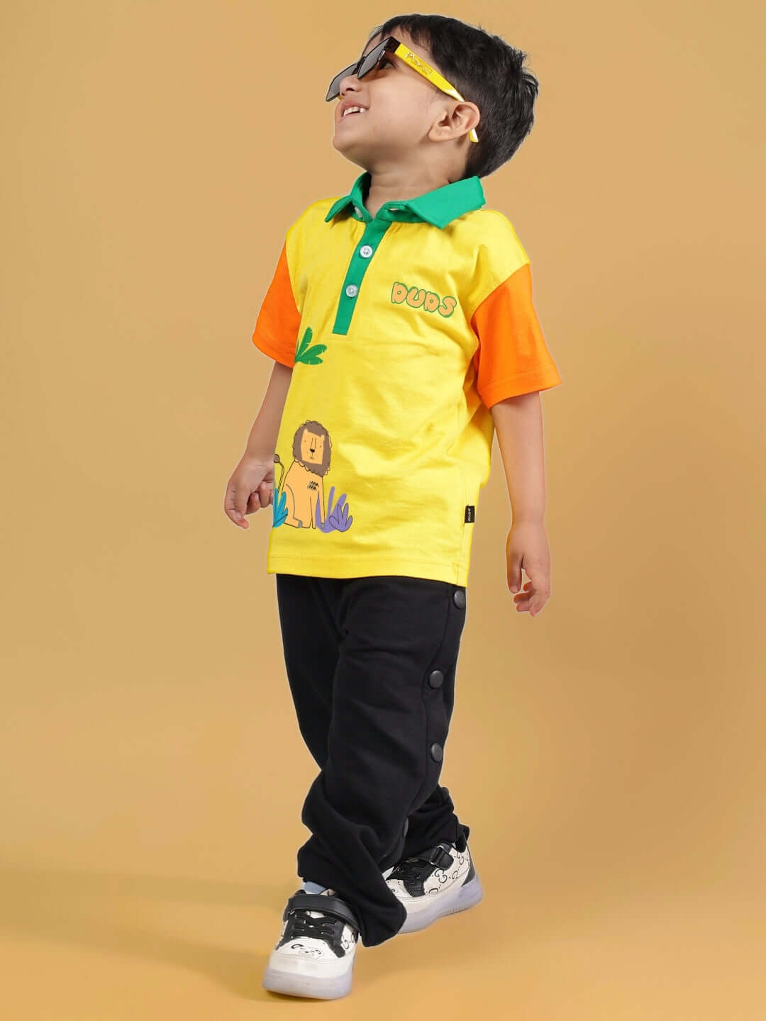 Child wearing DIBRU CO-ORD FOR BOYS & GIRLS YELLOW-BLACK outfit with yellow top and black pants, smiling on a light brown background.