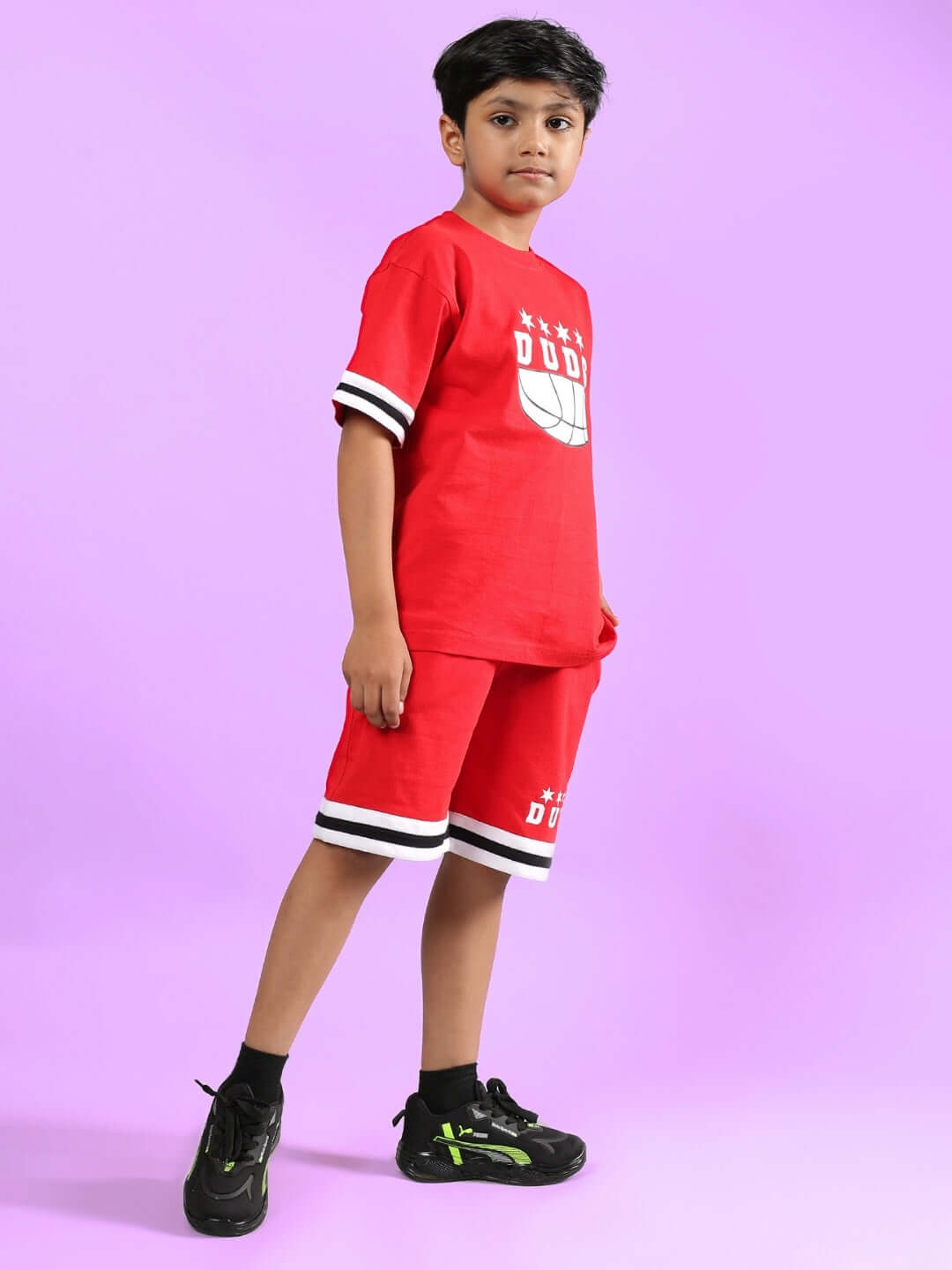 A child wearing the DIGGIN CO-ORD FOR BOYS & GIRLS RED outfit by DUDS in front of a purple background, featuring a red T-shirt and shorts.