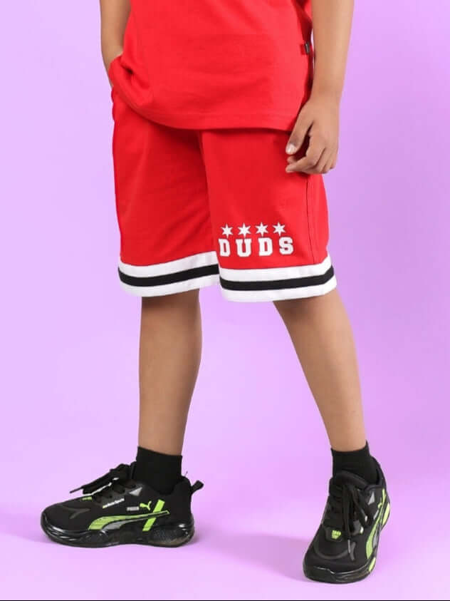 DIGGIN SHORTS FOR BOYS & GIRLS RED modeled by child wearing sneakers, standing on purple background.