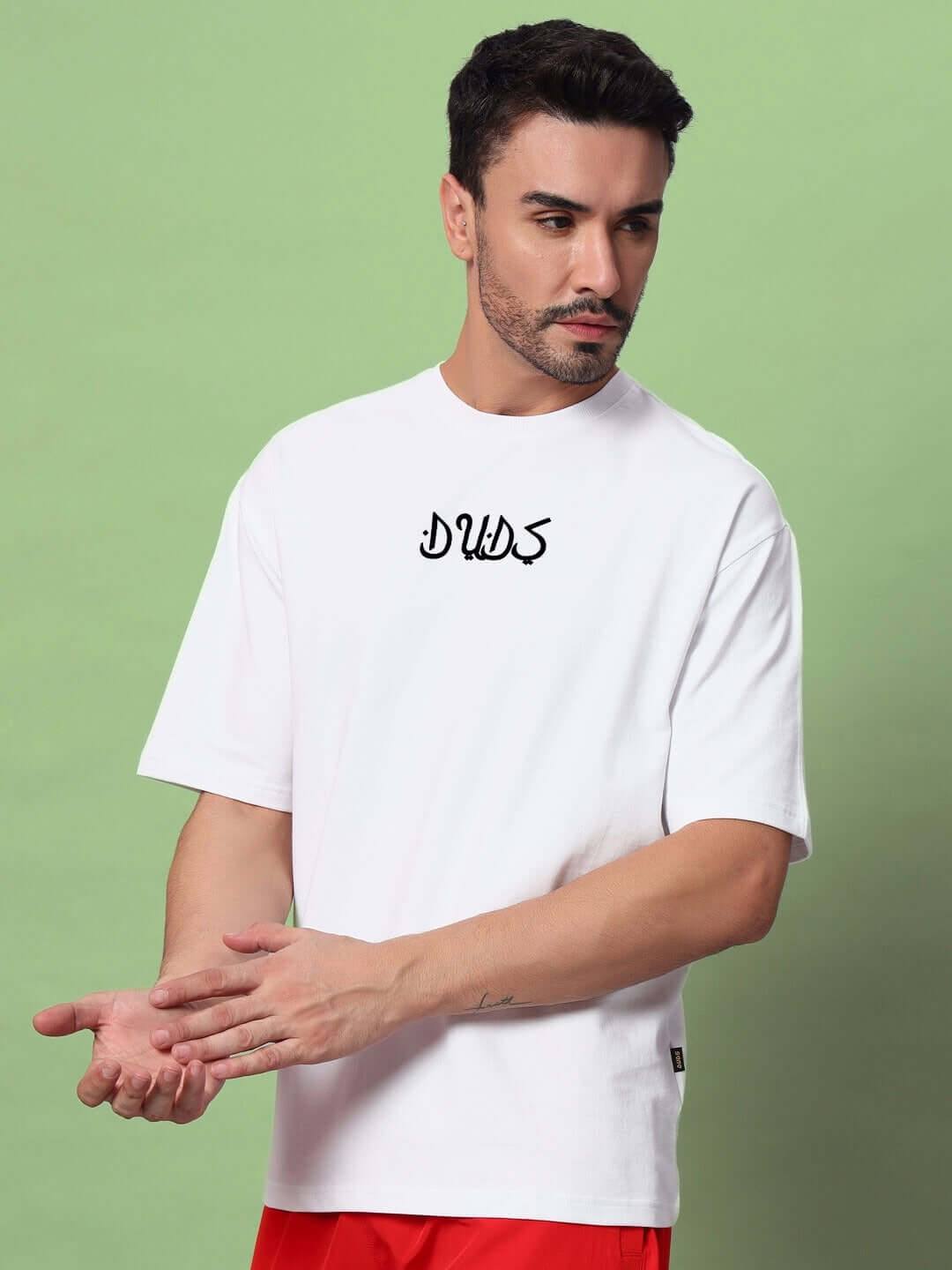 Model wearing white oversized T-shirt made from premium cotton French terry, featuring 'DUDS' text, against a green background.