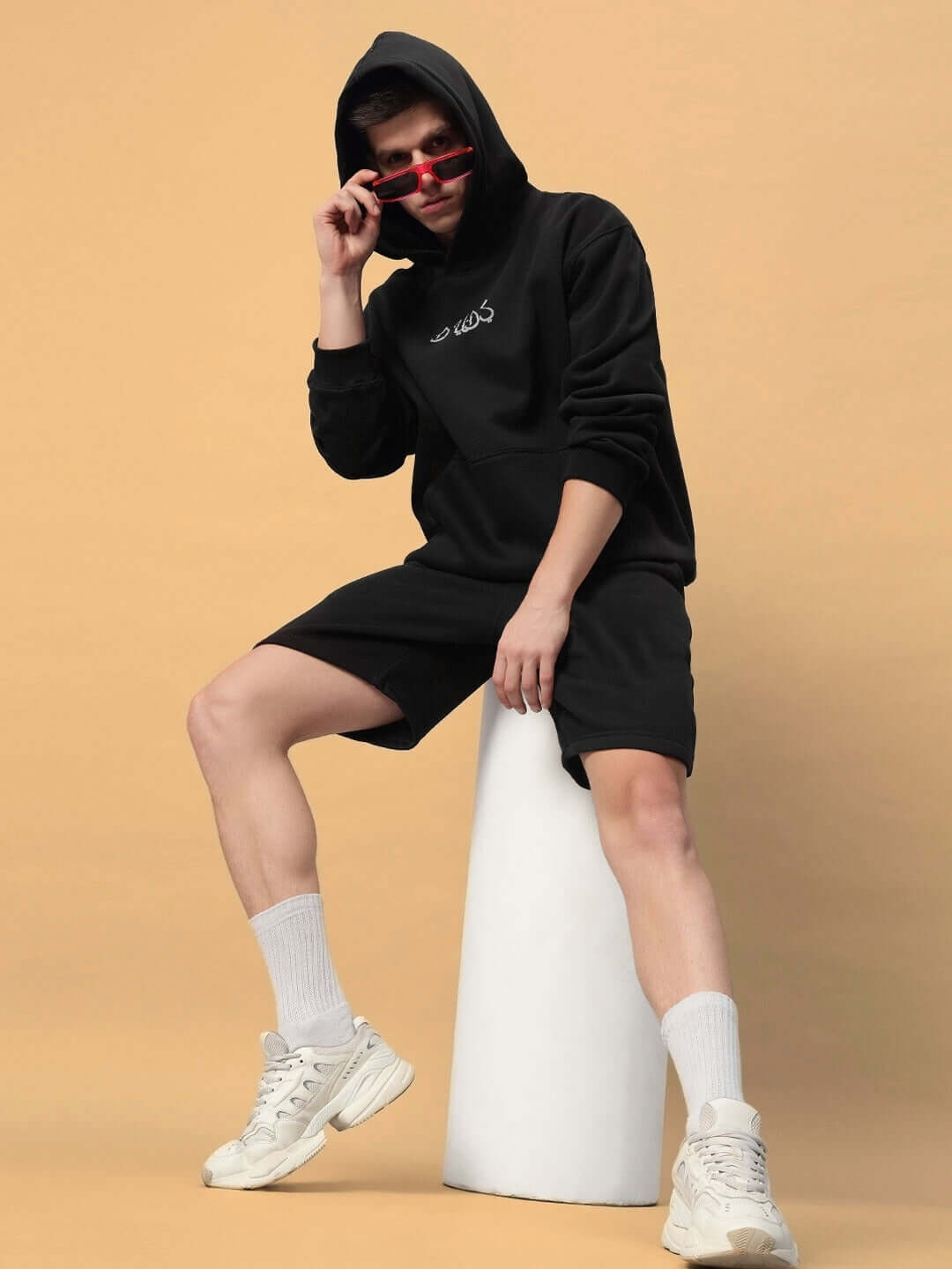Unisex DIMENSION COTTON FLEECE CO-ORD BLACK set with hoodie and shorts, showcasing street style on a model wearing sunglasses.