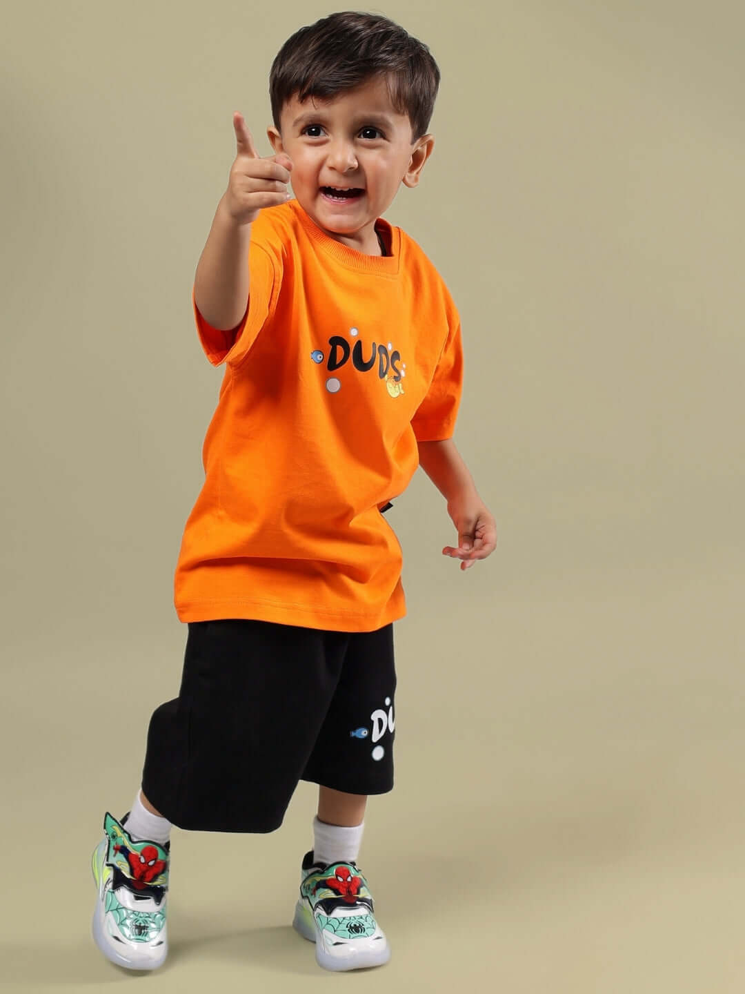 Child wearing black DIVING BEAR SHORTS FOR BOYS & GIRLS with orange shirt, smiling and pointing. Shorts made by DUDS, customizable fit available.