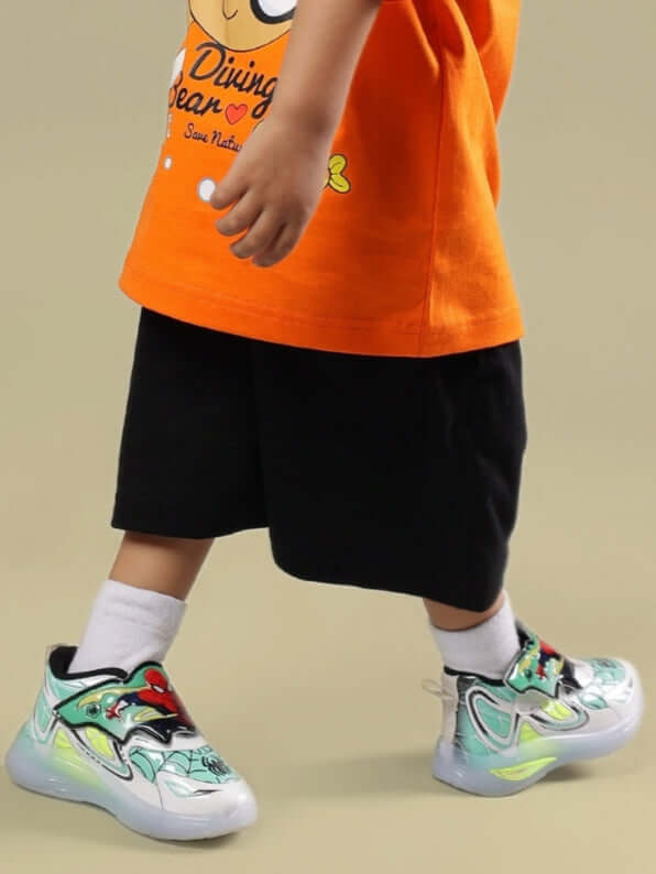 Child wearing Diving Bear Shorts for Boys & Girls Black with colorful sneakers and orange shirt.