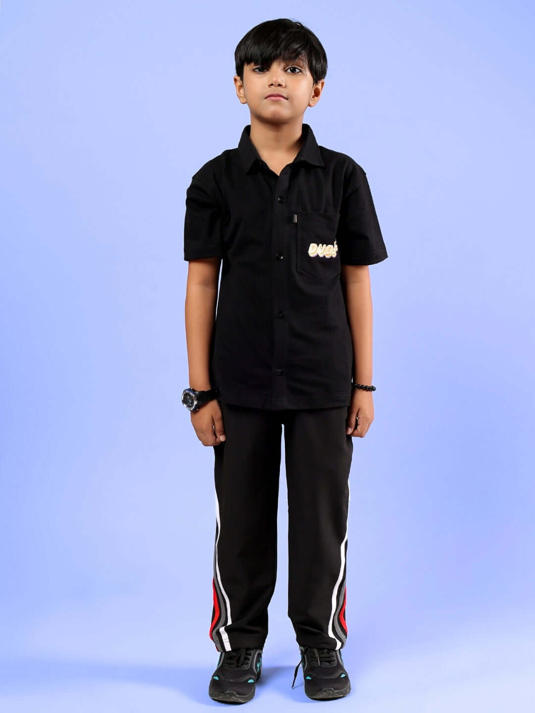 Young boy wearing DOBBIN JOGGER FOR BOYS & GIRLS BLACK with a matching black shirt on a blue background.