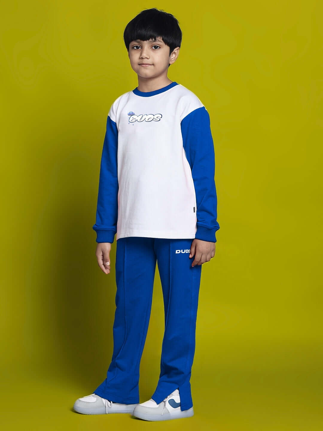 Child wearing white-blue Doraemon co-ord set featuring relaxed fit joggers and a long sleeve top, against a yellow background.
