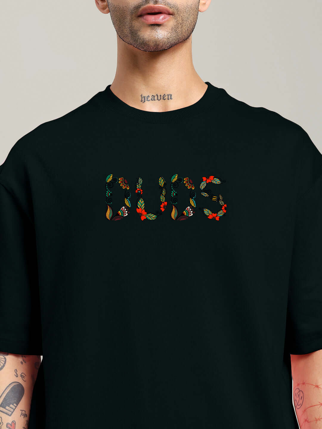 Close-up of black Dragonfly oversized t-shirt with colorful floral design and visible tattoos on arms and neck.