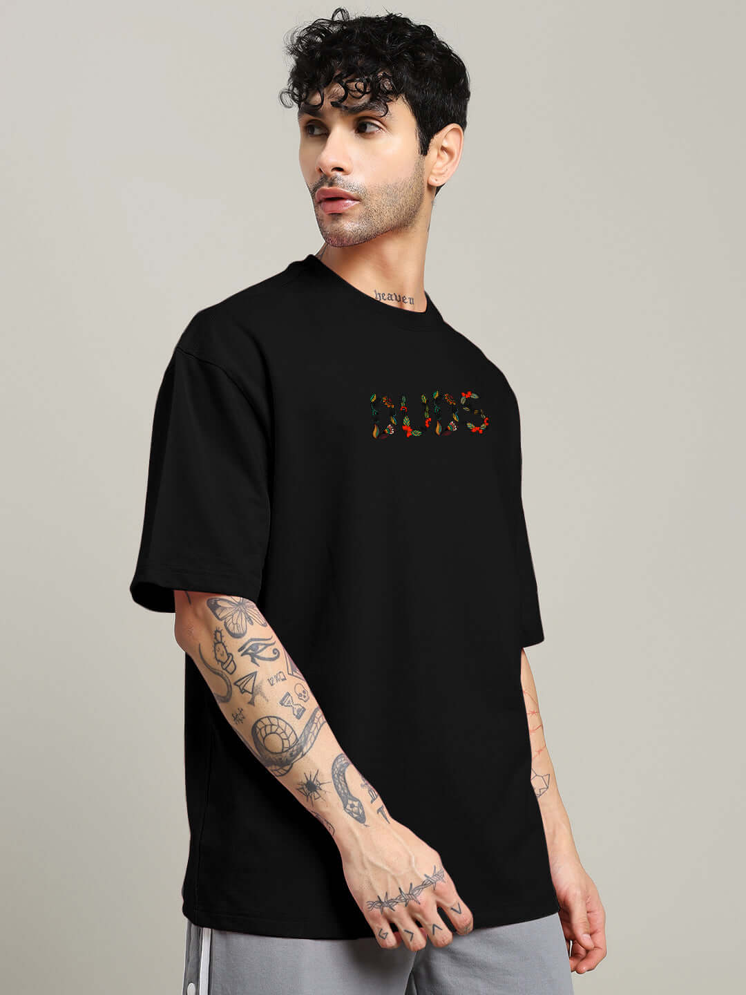 Young man wearing a black dragonfly oversized t-shirt made of premium cotton with tattoos, showcasing casual style in a studio setting.