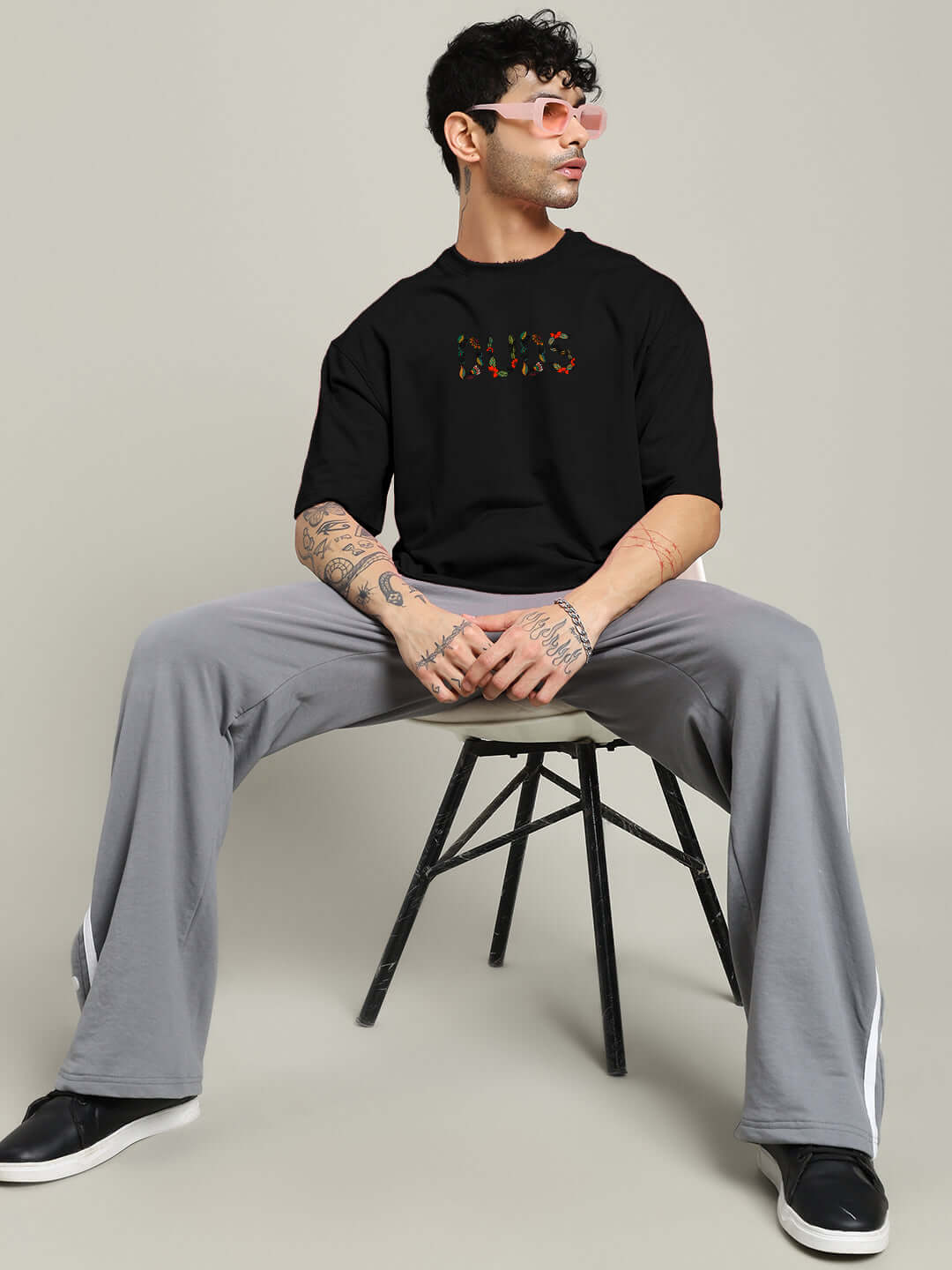 Model wearing Dragonfly Oversized Black T-Shirt made of premium cotton French terry fabric, sitting on a chair, styled casually.