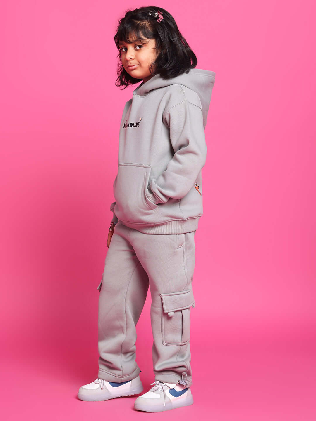 Child wearing grey DREAM FLEECE PANT with matching hoodie against pink background, showcasing comfortable and stylish kids' clothing.