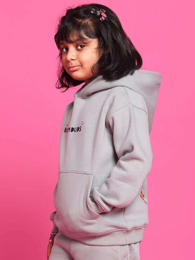 Child wearing grey DREAM oversized hoodie by DUDS against a pink background