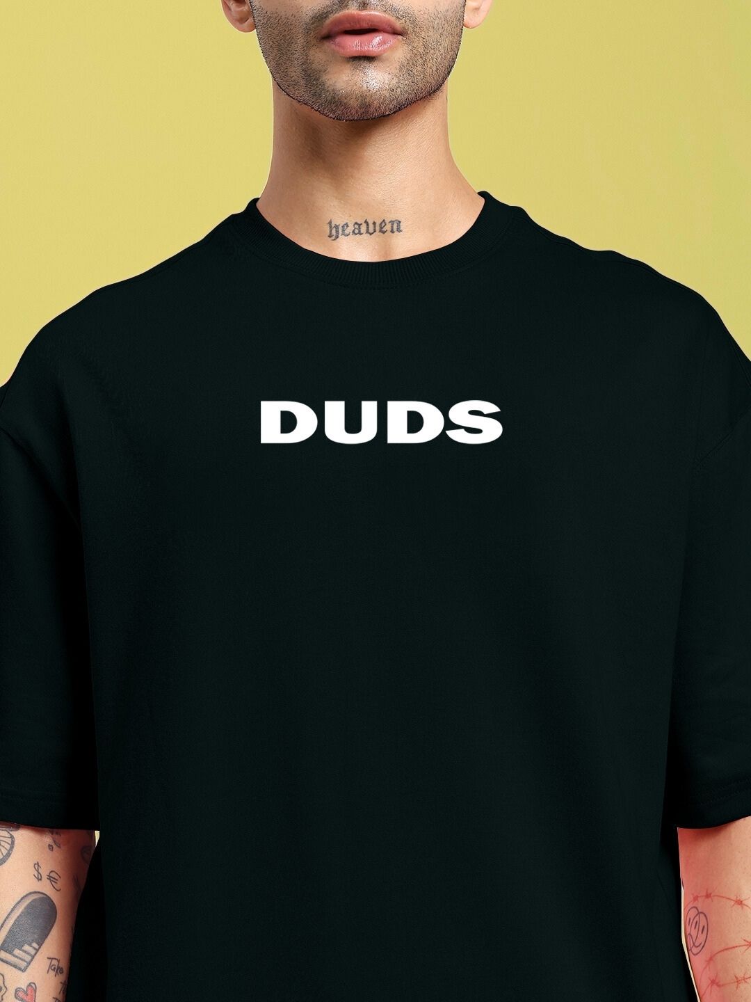 Man wearing DREAMLESS OVER-SIZED T-SHIRT BLACK with 'DUDS' text on chest, yellow background.