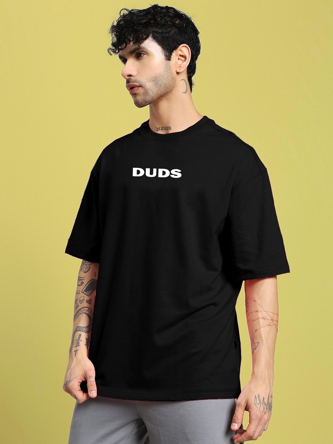 Model wearing DREAMLESS OVER-SIZED T-SHIRT BLACK showcasing relaxed fit and style against a yellow backdrop.