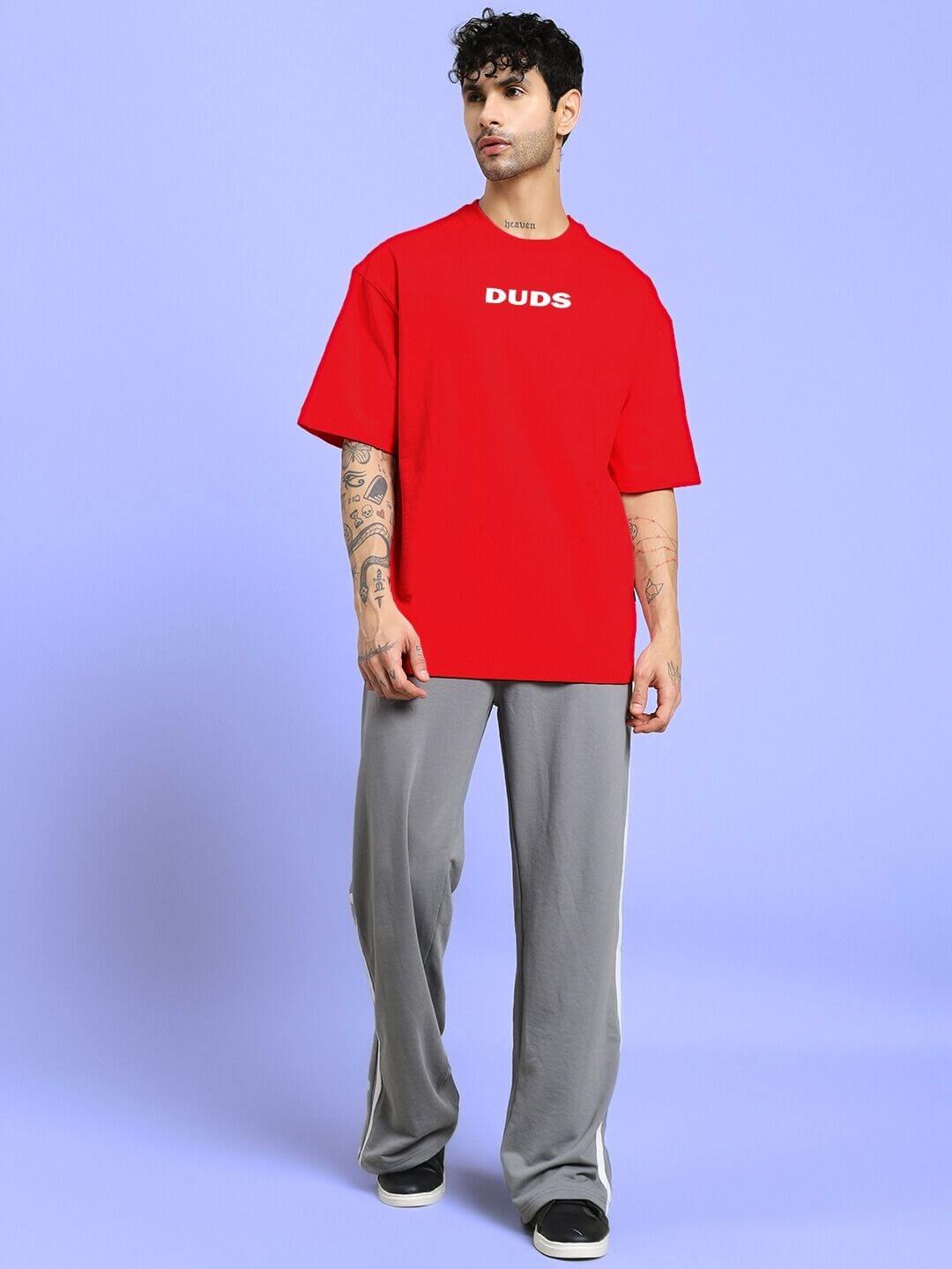 Man wearing DREAMLESS OVER-SIZED T-SHIRT RED in a modern streetwear style against a blue background.