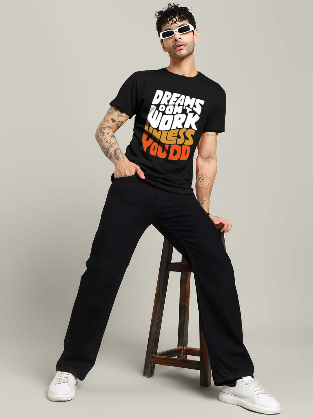 Man wearing DREAMS REGULAR FIT T-SHIRT BLACK, standing stylishly with sunglasses and sneakers, showcasing comfort and fashion.