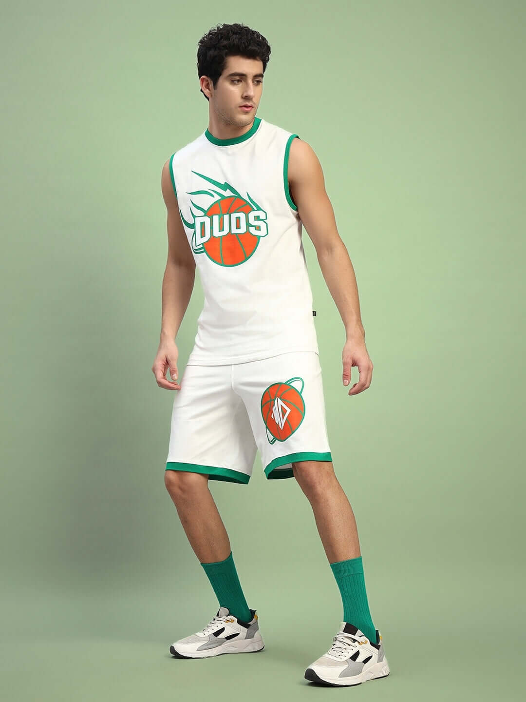 Model wearing DRIBBLE CO-ORD SET SLEEVELESS OFF WHITE, showcasing sleeveless top and shorts with green accents on a green background.