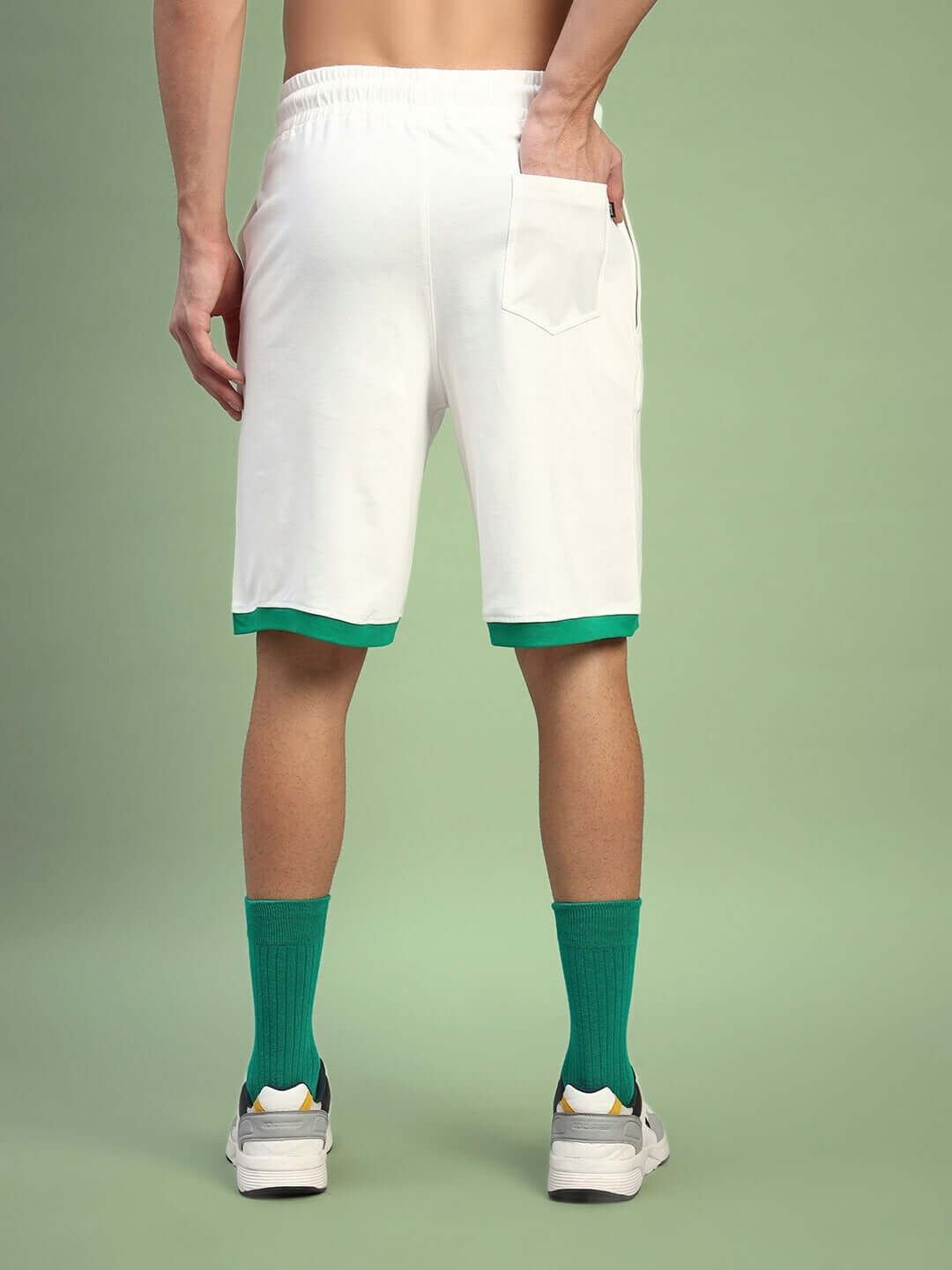 Back view of DRIBBLE SUMMER SHORTS OFF-WHITE with person wearing green socks and sneakers, showcasing stylish and comfortable summer wear.