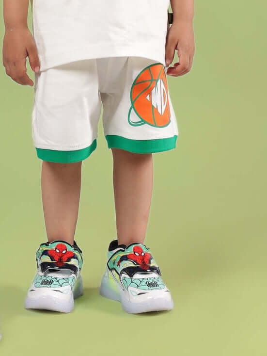 DRIBBLE SHORTS FOR BOYS & GIRLS OFF WHITE modeled by child with colorful sneakers, green background