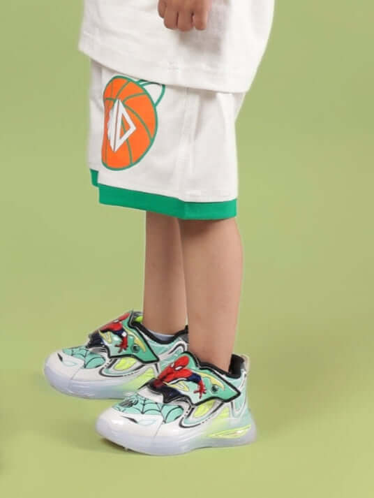 Child wearing DRIBBLE SHORTS FOR BOYS & GIRLS OFF WHITE with colorful sneakers on green background.