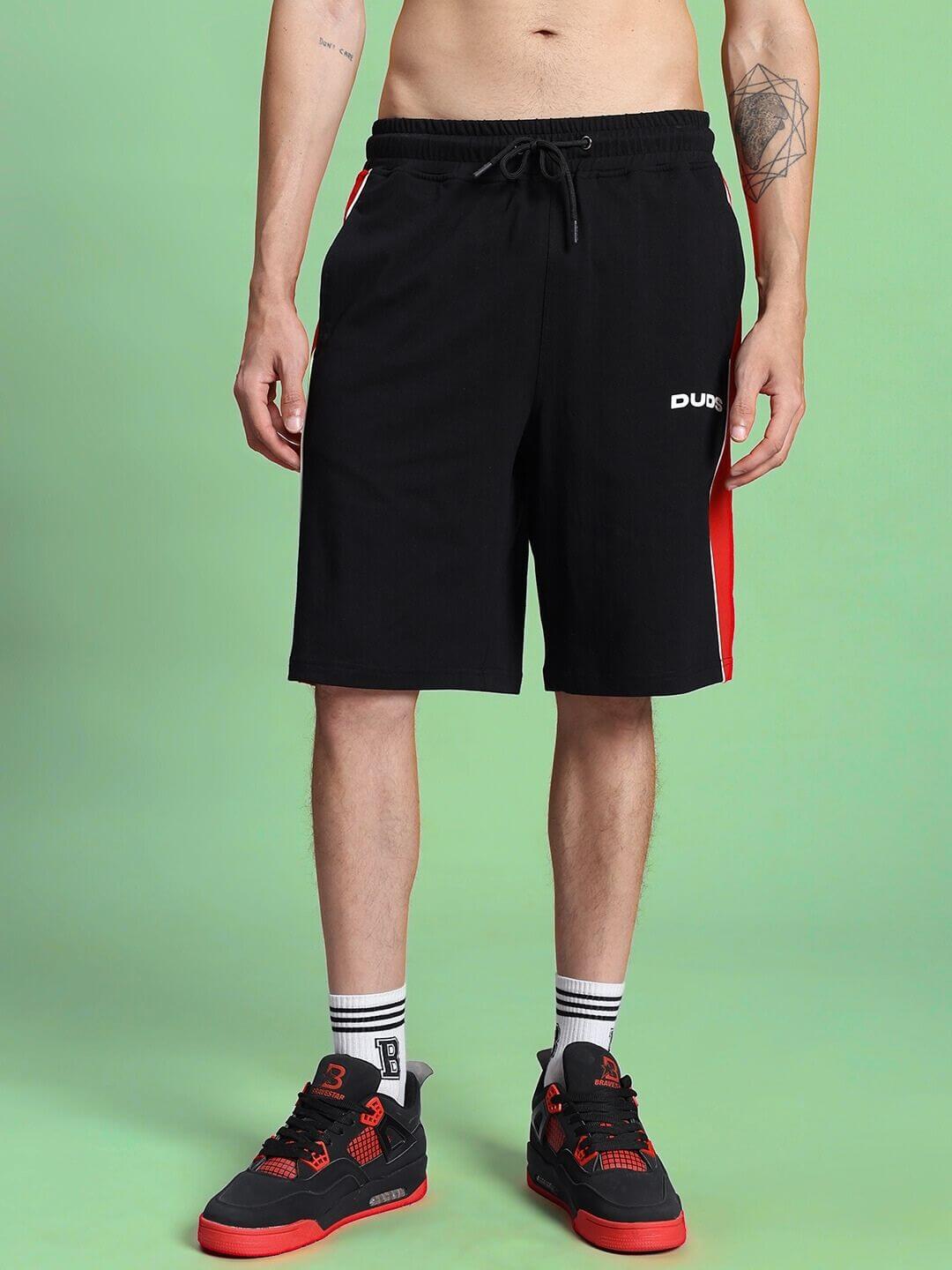 Man wearing DRIFT REGULAR FIT COTTON SHORTS BLACK standing against green background.