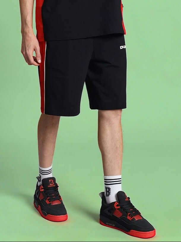 Person wearing DRIFT REGULAR FIT COTTON SHORTS BLACK with red sneakers on green background