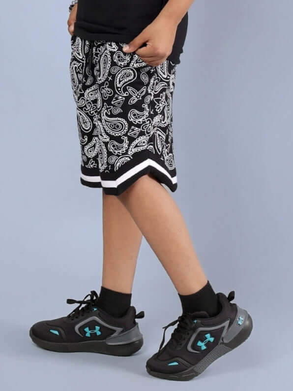 Child wearing black and white Drizzle Shorts for boys & girls with paisley pattern, paired with sneakers. Ideal summer wear.