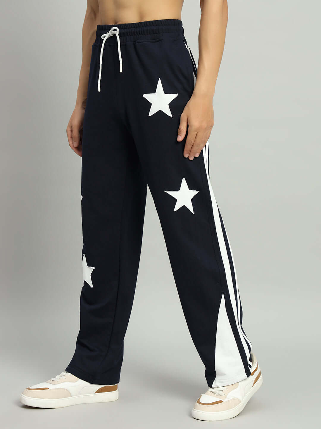 Navy blue joggers with white star pattern and side stripes, featuring a relaxed fit and drawstring waist, worn by a model with sneakers.