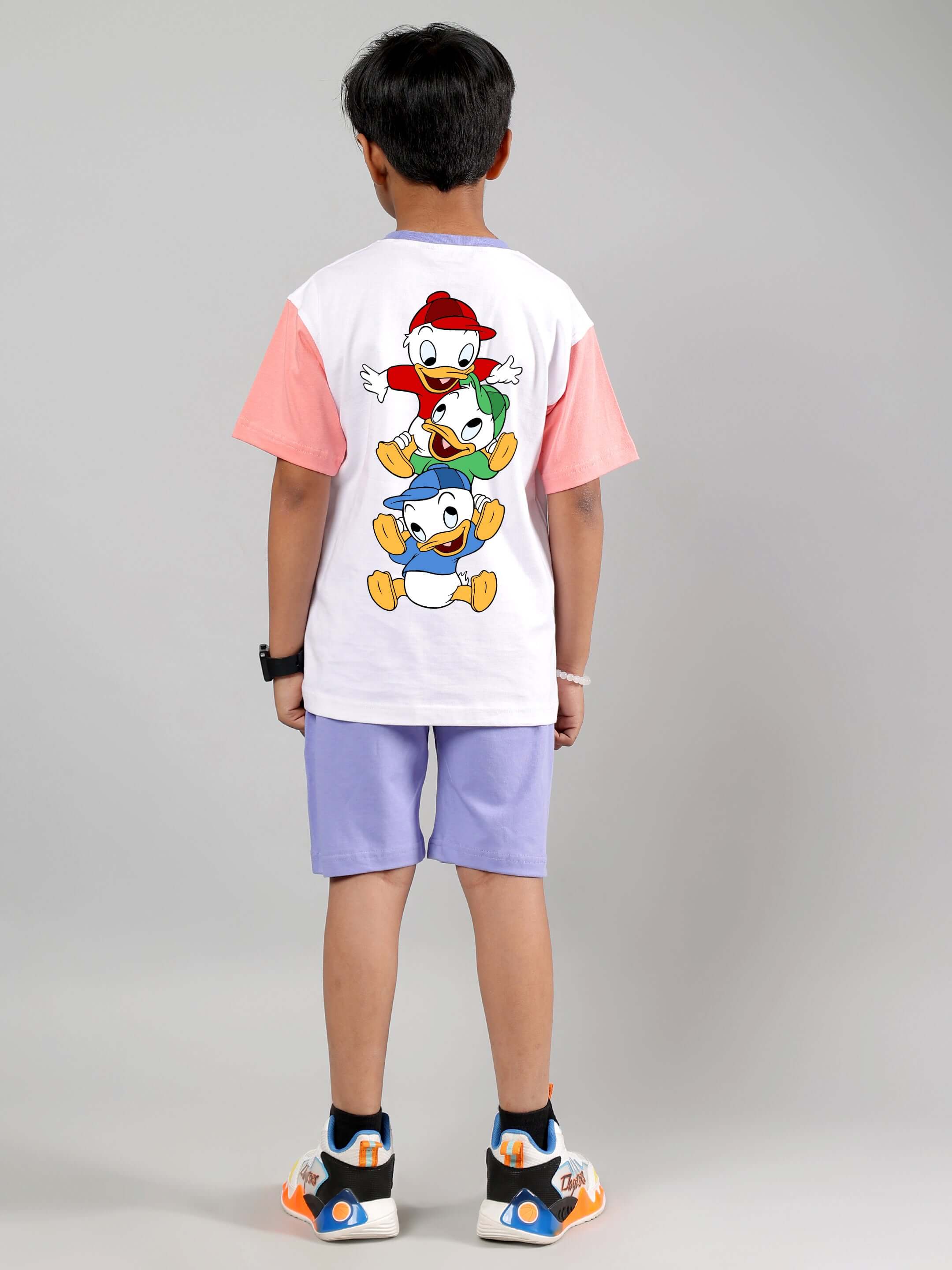 Child wearing DUCK PLAY CO-ORD FOR BOYS GIRLS WHITE LAVENDER featuring cartoon print, white shirt, and lavender shorts, back view.