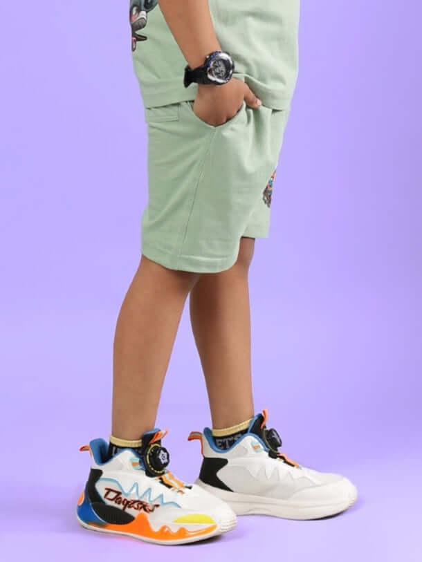 Child wearing DUCK TALES SHORTS FOR BOYS & GIRLS NYANZA GREEN standing with colorful sneakers on a purple background