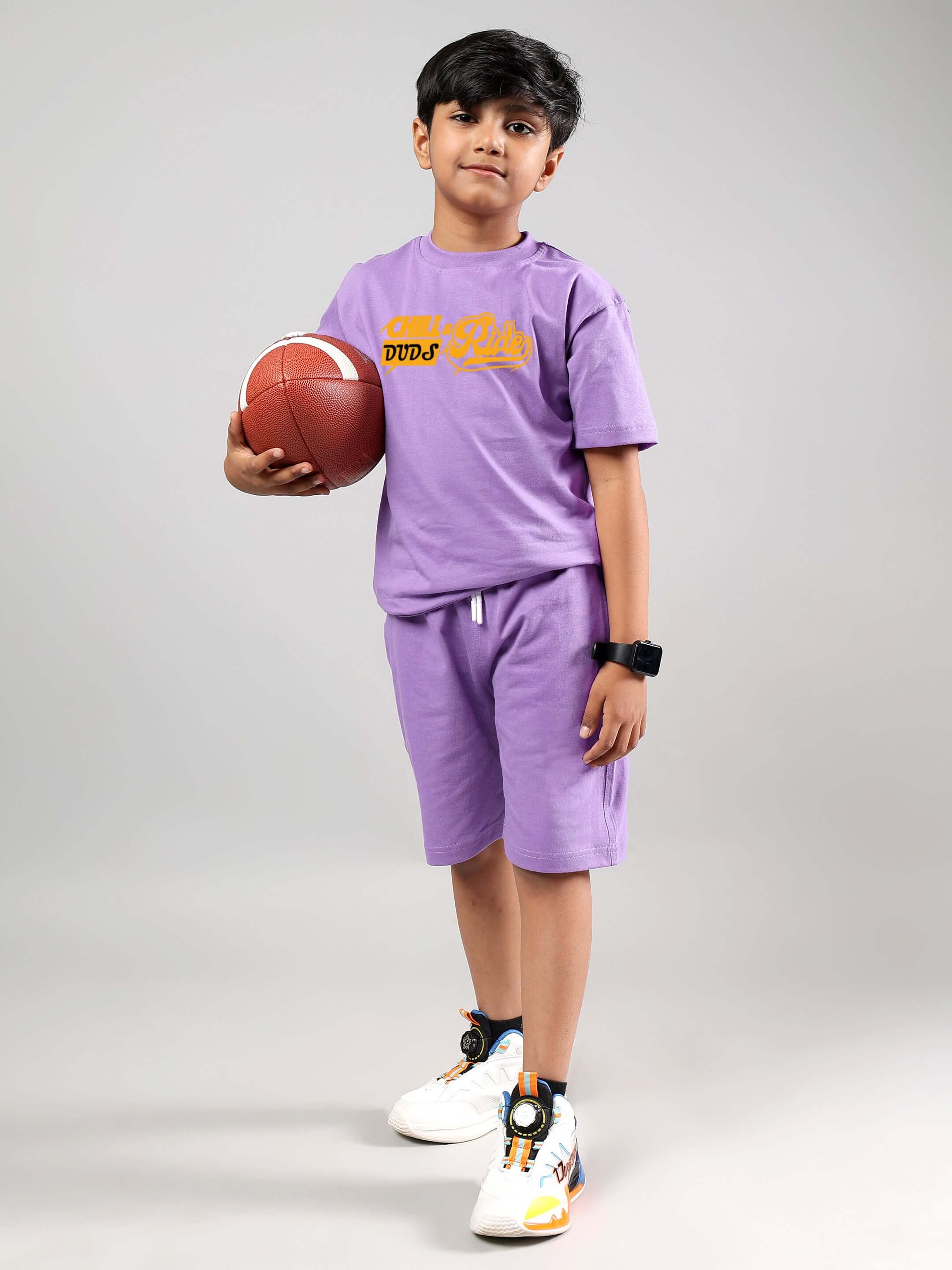 Boy wearing DUDS Chill & Ride lavender t-shirt and shorts, holding basketball, standing confidently.
