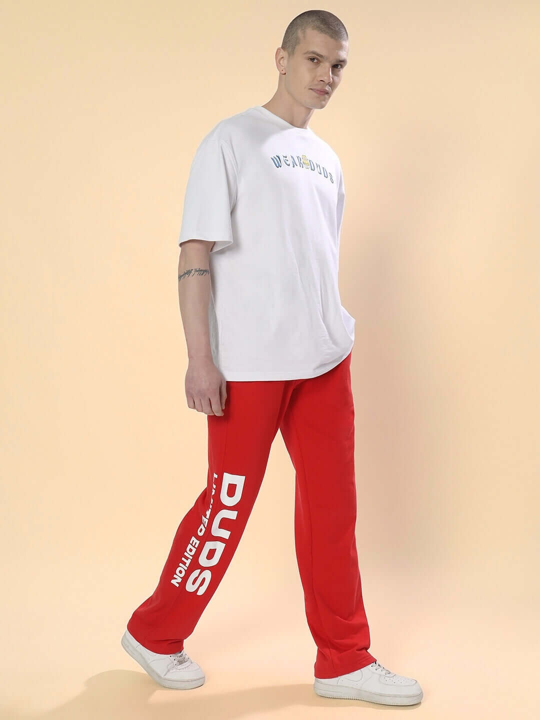 Man wearing DUDS limited edition red joggers and a white shirt, standing against a beige background.