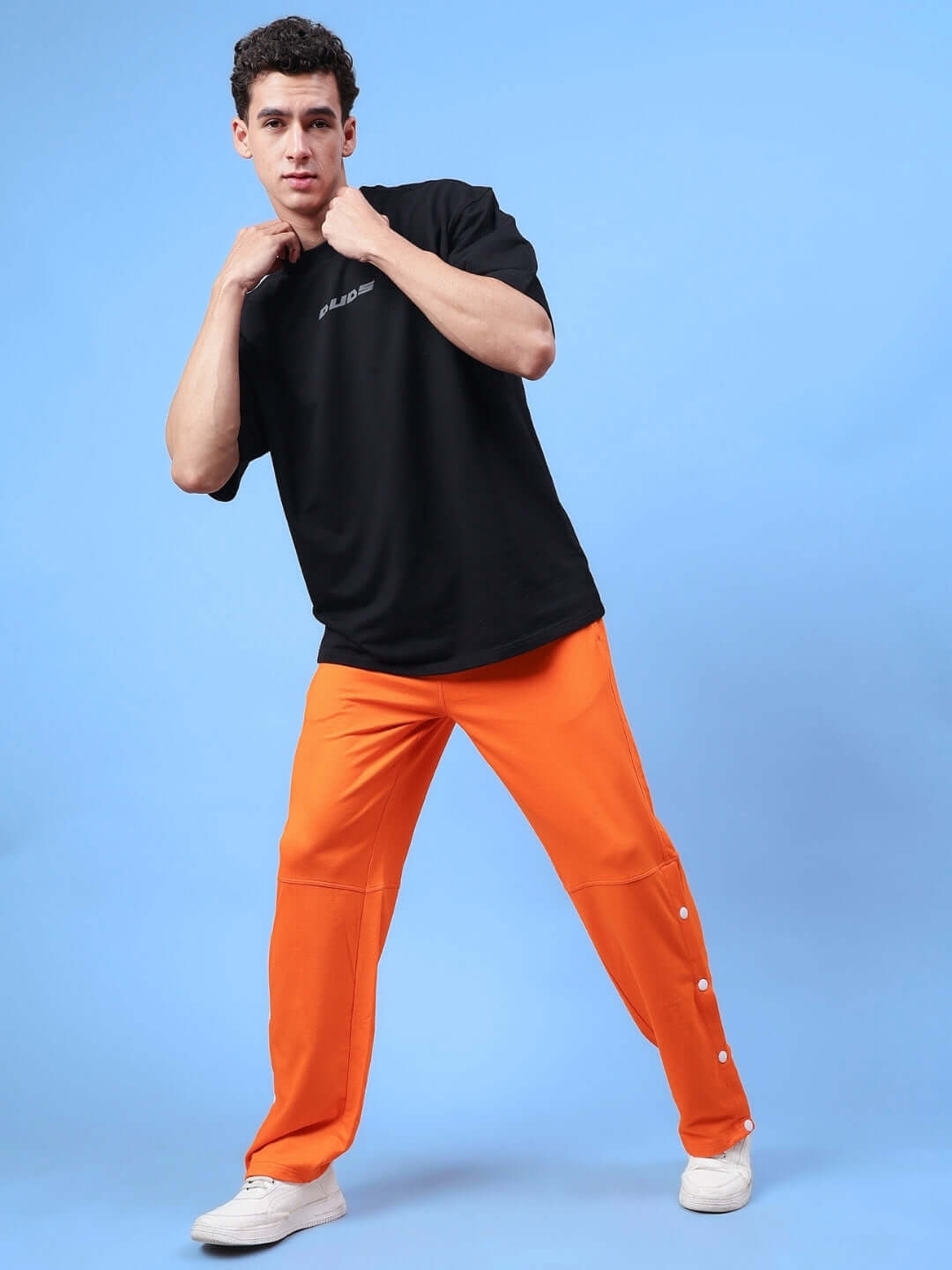 Model wearing DUDS Racer Joggers in orange, demonstrating comfort and style, paired with a black t-shirt and white sneakers.