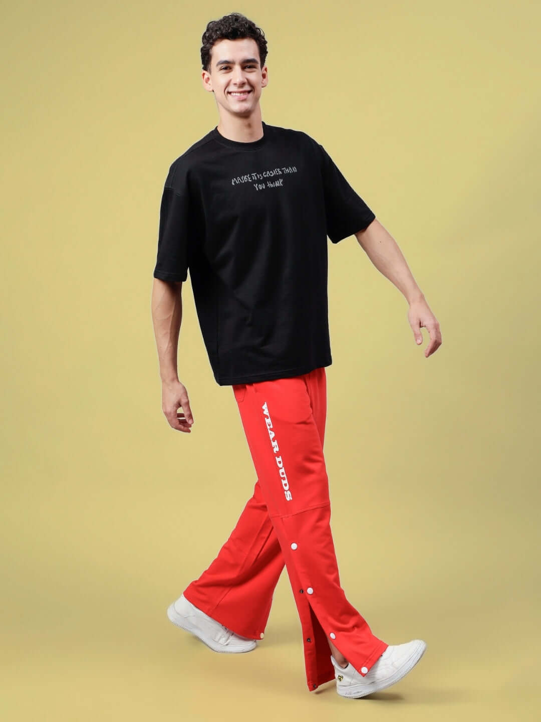 Model wearing red DUDS Racer Joggers with black t-shirt against a yellow background, showcasing stylish made-to-order pants.