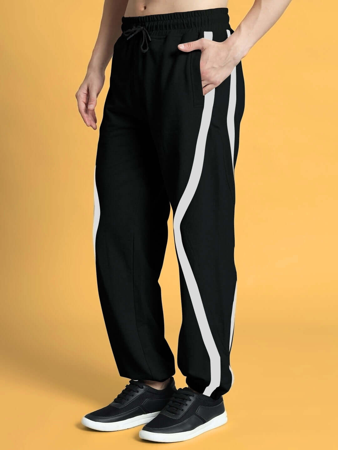 Man wearing black DUDS FRAME joggers with white stripes, showcasing comfort fit and style against a yellow background.