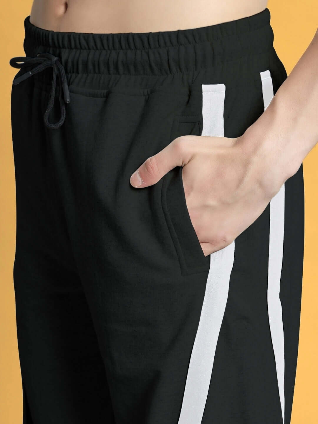 Close-up of black DUDS FRAME joggers with a hand in the pocket, showcasing white side stripes and adjustable drawstring waistband.