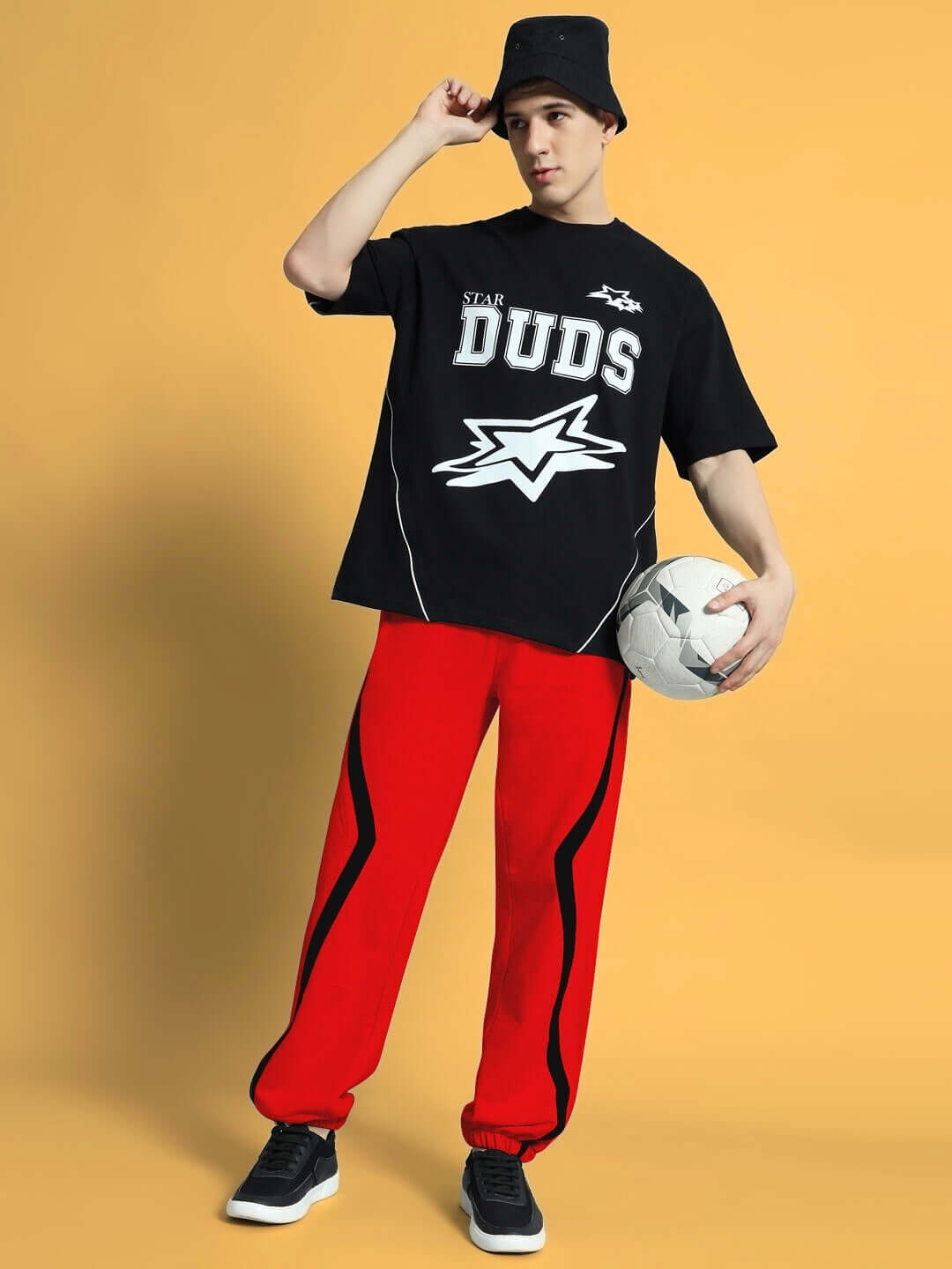 Model wearing DUDS Frame Joggers in red, holding a soccer ball, with customizable fit option made by experienced tailors.