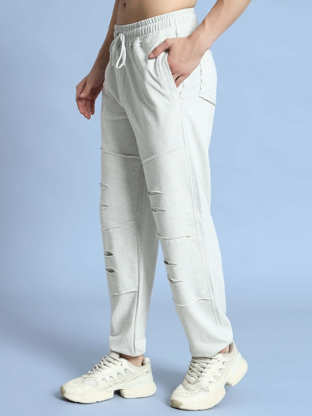 Model wearing melange grey DUDS Graze joggers with a casual fit and ripped design, styled with white sneakers on a blue background.