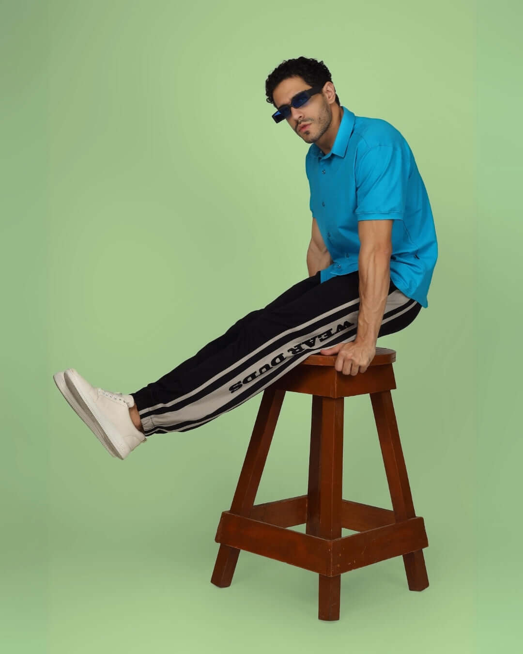 Model wearing DUDS HD Contrast Panel Joggers in black grey and blue polo on wooden stool, showcasing stylish casual wear.
