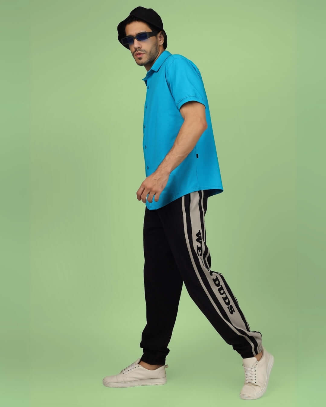 Man wearing DUDS HD contrast panel joggers in black and grey with casual blue shirt and white sneakers, showcasing modern fashion style.
