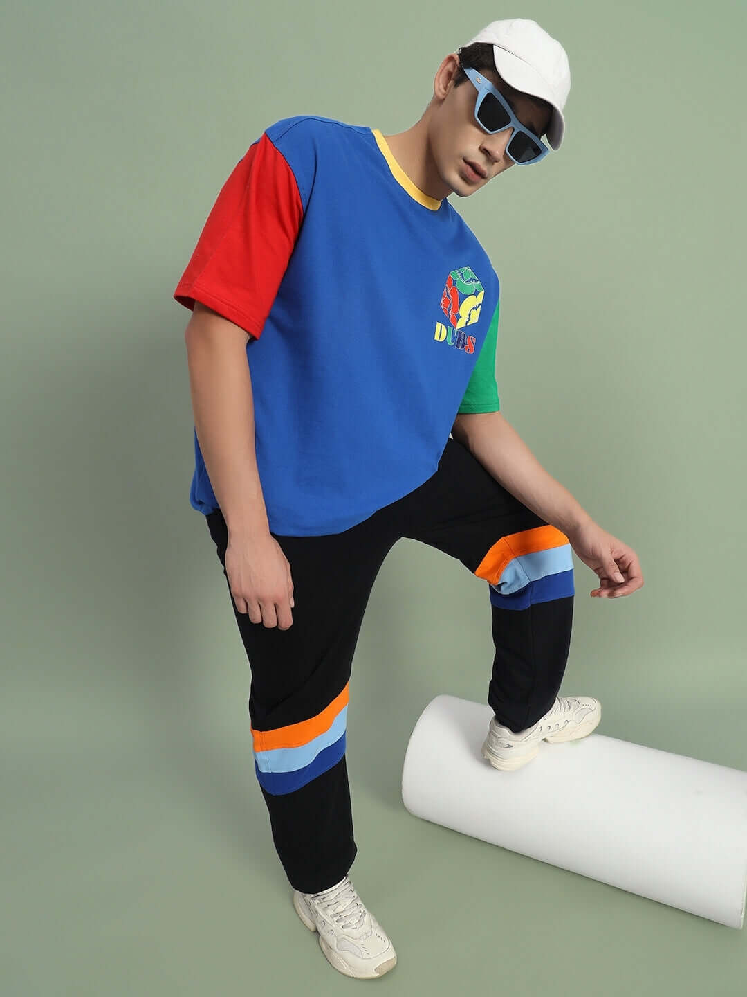 Model showcasing DUDS Jasper Joggers in black, featuring colorful side stripes, styled with a multicolored t-shirt and sunglasses.