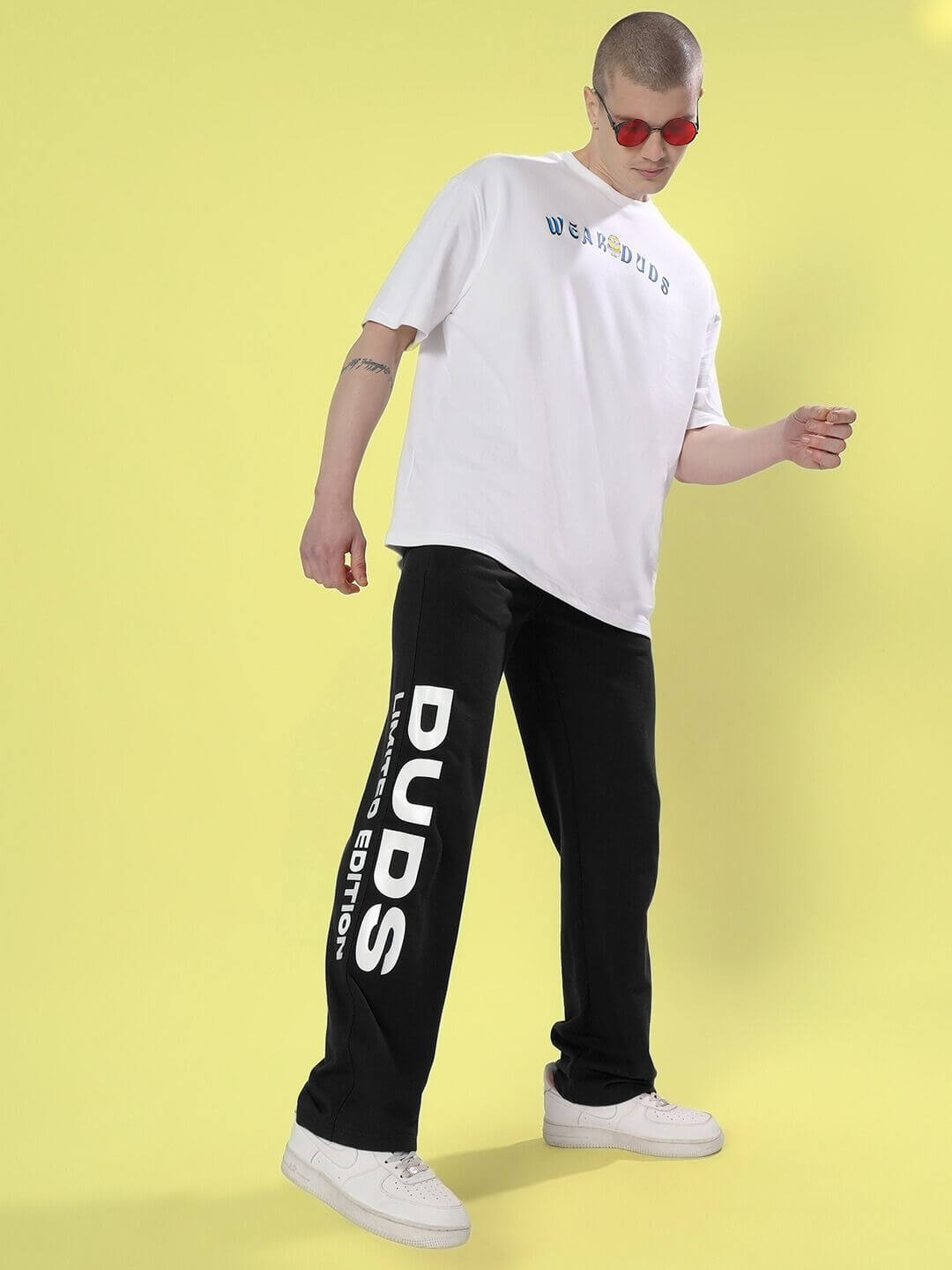 Model wearing DUDS Limited Edition Jogger in black with white tee and red sunglasses on a yellow background.