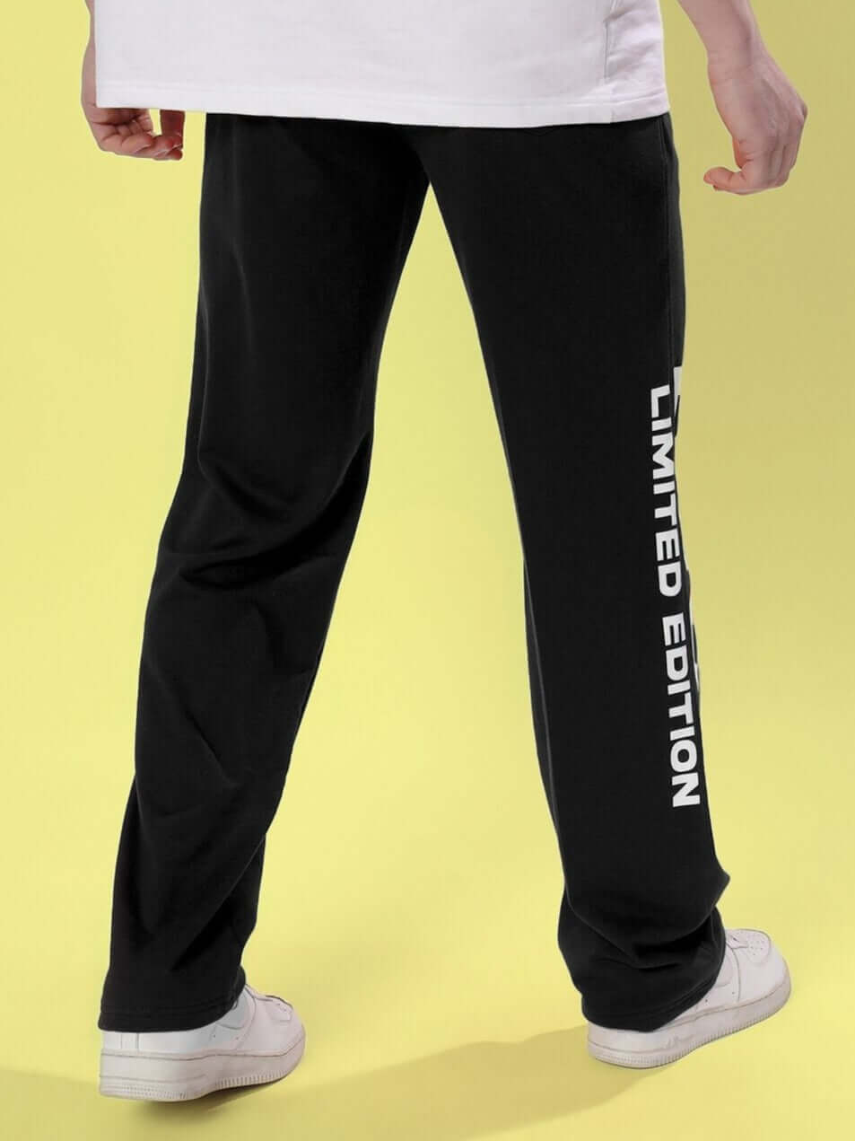 Rear view of DUDS Limited Edition Black Jogger with white lettering, worn with white sneakers on a yellow background.
