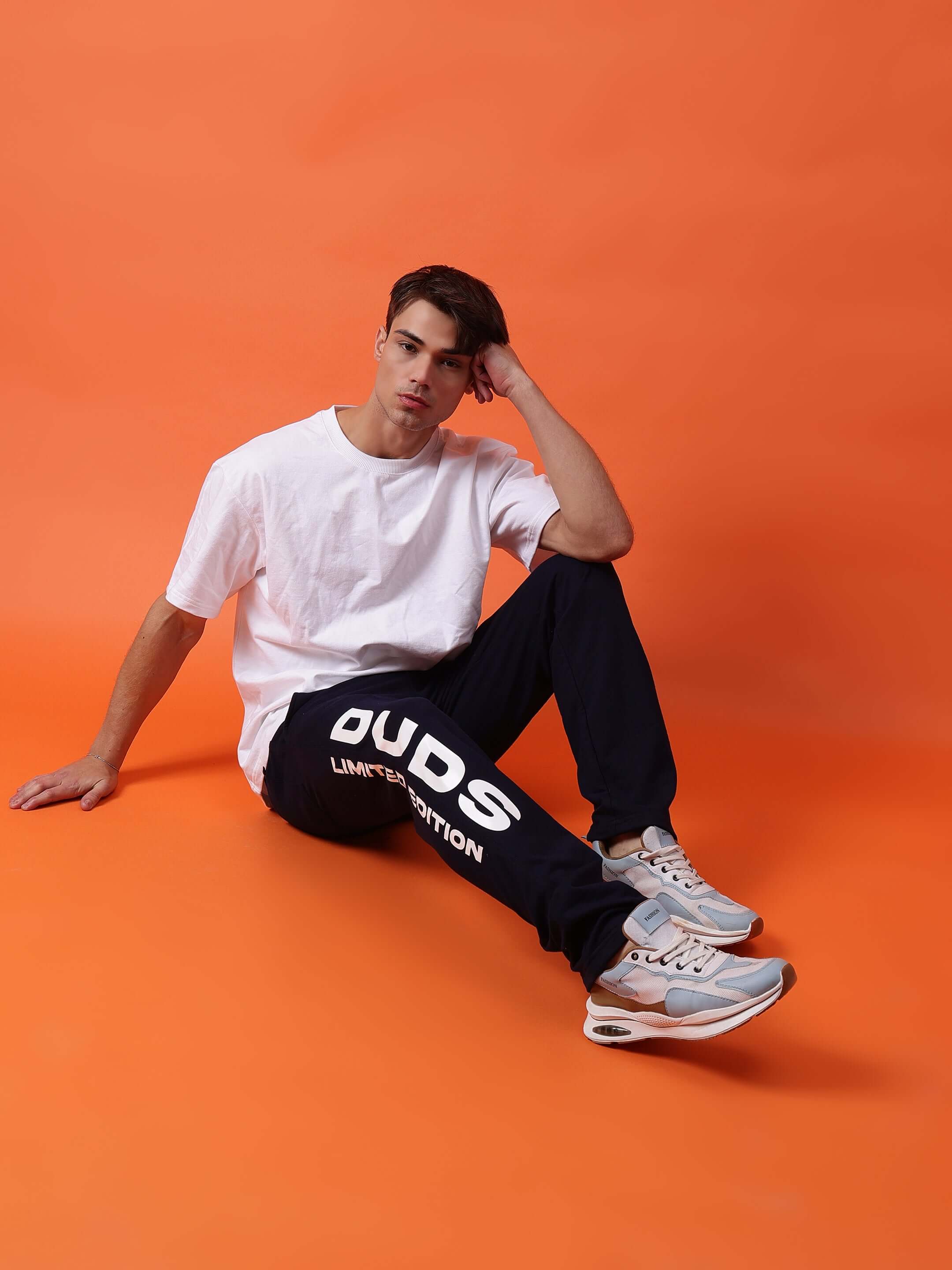 Model wearing DUDS Limited Edition Jogger in navy blue, sitting against an orange background, showcasing casual style and comfort.